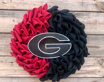May include: A red and black burlap wreath with a black and white "G" in the center. The wreath is made of burlap and is decorated with a black and white "G".