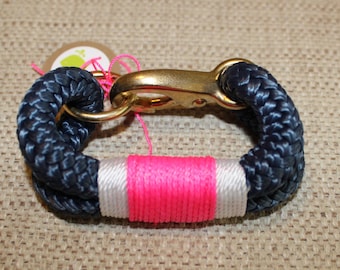 May include: A navy blue rope bracelet with a gold clasp and a pink and white striped band.