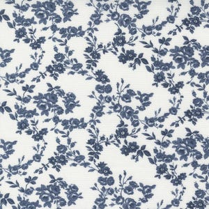 May include: White fabric with a repeating pattern of blue floral bouquets and vines. The flowers are a deep blue, and the leaves are a darker shade of blue. The background is a clean white, creating a contrast that highlights the floral design.