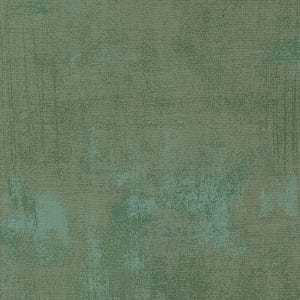 May include: A close-up of a textured fabric with a mottled appearance. The color palette is dominated by shades of green, with areas of lighter teal and darker olive tones. The fabric has a distressed, vintage look.