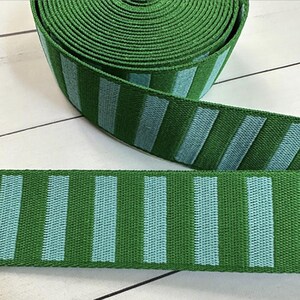 May include: Green and blue striped ribbon with a woven texture. The ribbon is rolled up and the stripes are vertical.
