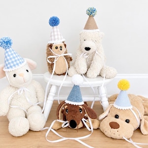 Pode incluir: Uma cole&ccedil;&atilde;o de cinco animais de pel&uacute;cia, incluindo um cordeiro, um ouri&ccedil;o, um urso polar, um dachshund e um c&atilde;o, cada um usando um chap&eacute;u de festa em miniatura. Os chap&eacute;us apresentam v&aacute;rios padr&otilde;es como xadrez azul, riscas e cores s&oacute;lidas com pompons.