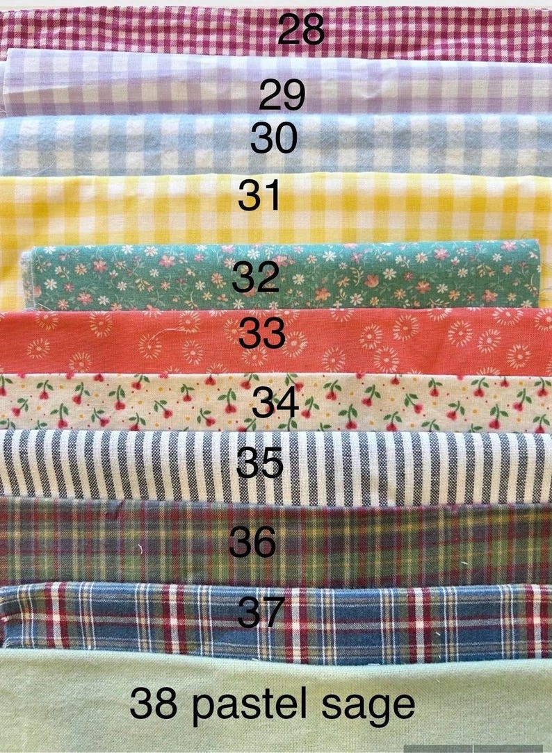 Pode incluir: Uma cole&ccedil;&atilde;o de onze amostras de tecido dobradas empilhadas verticalmente, numeradas de 28 a 38. Os padr&otilde;es incluem xadrez vichy, estampas florais, listras e xadrez em v&aacute;rias cores como vermelho, lavanda, azul, amarelo, verde e branco.