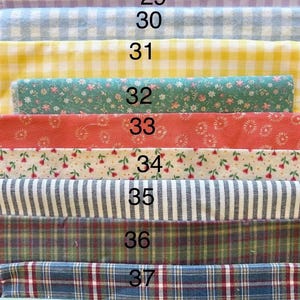 May include: A collection of eleven fabric swatches stacked vertically, labeled 28 through 38. Patterns include gingham in maroon, lavender, blue, and yellow, floral prints in green, coral, and white, black and white stripes, and various plaid designs.