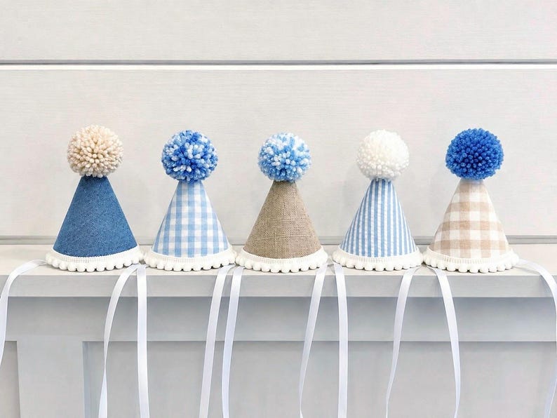 Pode incluir: Cinco chap&eacute;us de festa em forma de cone com acabamento de pompom branco na base e um grande pompom de l&atilde; no topo. Os chap&eacute;us apresentam v&aacute;rios padr&otilde;es, incluindo ganga azul s&oacute;lida, xadrez vichy azul e branco, linho bege, riscas.
