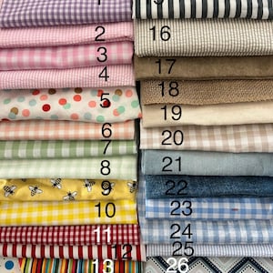 May include: A collection of twenty-seven folded fabric swatches arranged in two columns, featuring various patterns including gingham, stripes, polka dots, and bee prints in colors such as lavender, pink, yellow, blue, red, green, and brown.