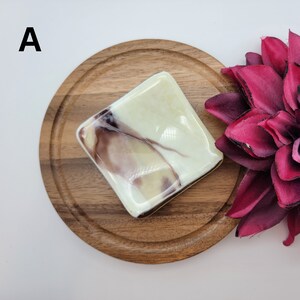 Puede incluir: Un plato cuadrado de vidrio marmoleado blanco y marr&oacute;n sobre una base de madera. El plato tiene un patr&oacute;n marmoleado marr&oacute;n claro y blanco con un toque de morado.