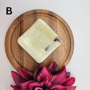Puede incluir: Una pastilla de jab&oacute;n cuadrada de color amarillo claro y marr&oacute;n con un remolino de marr&oacute;n oscuro en una bandeja de madera.
