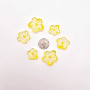 May include: A group of seven yellow glass flower-shaped embellishments on a white background. The flowers are translucent and have a yellow outline.