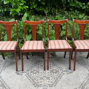 May include: Four wooden dining chairs with red and white striped upholstery. The chairs have a classic design with a curved back and a slightly flared seat.