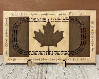 May include: Wooden Canadian flag game board with a maple leaf design and the names of each province and territory. The board is on a stand and has the text "We Stand On Guard For Thee" on the right side.
