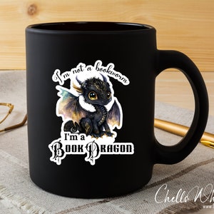 May include: Black ceramic mug with a white sticker featuring a cartoon dragon and the text "I'm not a bookworm I'm a Book Dragon".