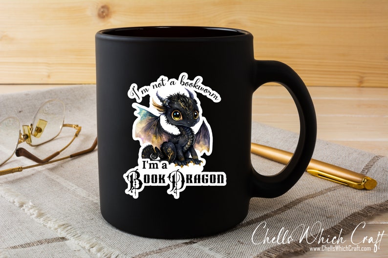 May include: Black ceramic mug with a white sticker featuring a cartoon dragon and the text "I'm not a bookworm I'm a Book Dragon".