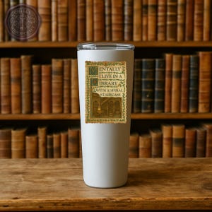 May include: White insulated tumbler with a clear lid. The tumbler features a decorative sticker with the text "Mentally I live in a library with a spiral staircase" in a vintage style. The background shows a bookshelf.