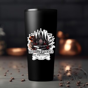 Puede incluir: Un vaso de acero inoxidable negro con una pegatina blanca que muestra una catedral g&oacute;tica, libros y el texto "Las historias para dormir son mis favoritas".