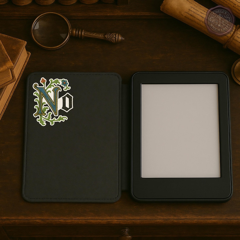 May include: Black e-reader with a decorative cover featuring the letters "N" and "O" in a floral design. The e-reader is open, displaying a blank screen. The cover is open, revealing the e-reader.