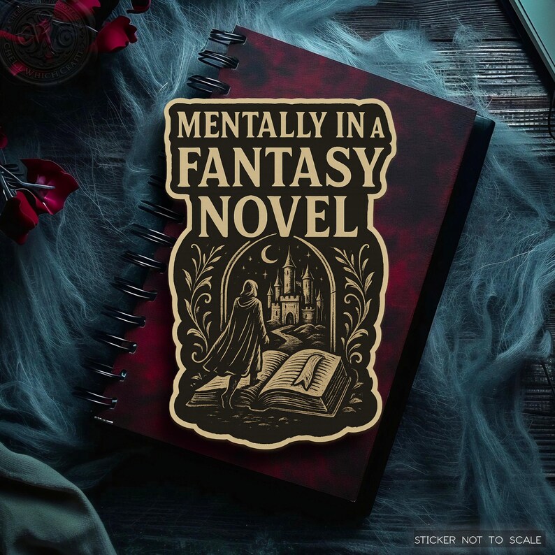 May include: A sticker with the text "MENTALLY IN A FANTASY NOVEL" in a decorative font. The sticker features an illustration of a person in a cloak walking towards a castle, with an open book in the foreground. The sticker is on a red notebook.