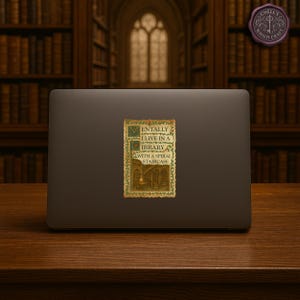 May include: A sticker on a laptop featuring the text "Mentally I live in a library with a spiral staircase." The sticker has a vintage design with green and gold accents, and an illustration of a library interior.