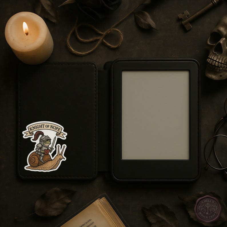 May include: A black e-reader with a matching cover featuring a sticker of a knight riding a snail, with the text "KNIGHT OF NOPE". A lit candle, a skull, and a key are visible in the background.