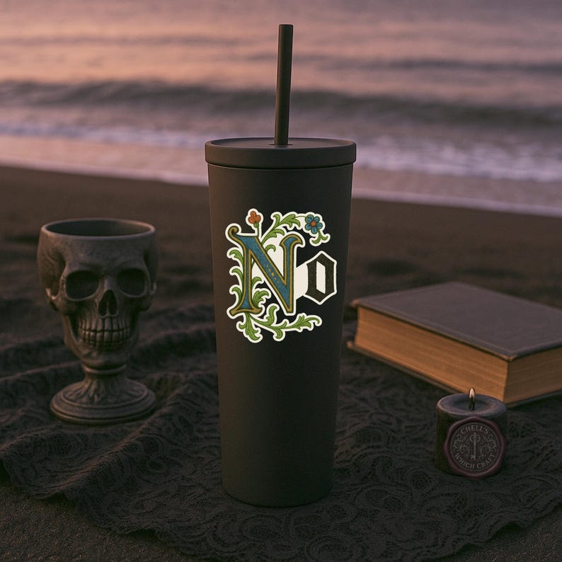 May include: A black tumbler with a straw, featuring a sticker with the word "No" in an ornate, vintage font. The design includes blue, green, and gold floral accents. A skull-shaped goblet, a book, and a candle are in the background.