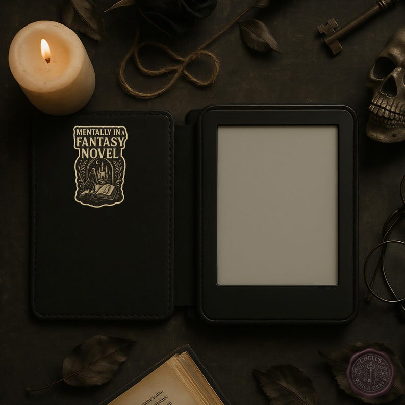 May include: Black e-reader with a cover featuring the text "MENTALLY IN A FANTASY NOVEL" and a graphic of a person reading. The scene includes a lit candle, a skull, a key, and other gothic-themed accessories.