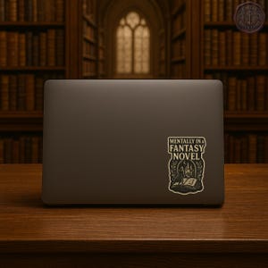 May include: A laptop with a sticker that reads "Mentally in a Fantasy Novel." The sticker features a detailed illustration of a person in a cloak, a book, and a castle. The laptop is on a wooden surface.