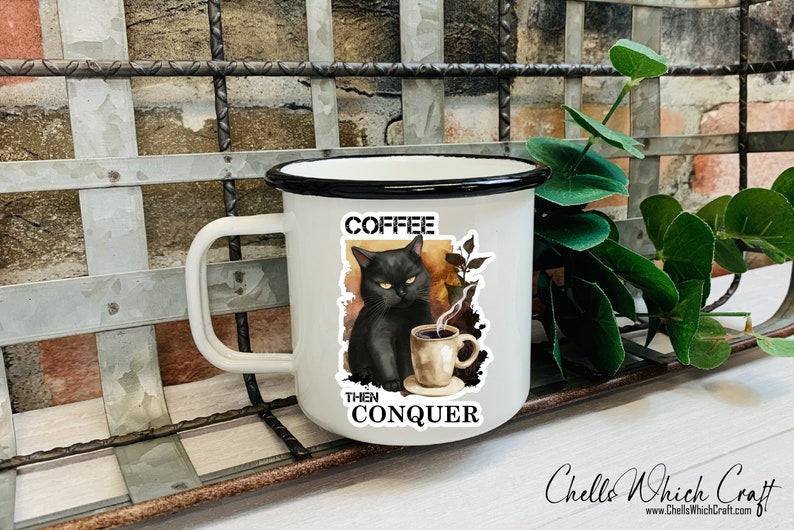 May include: White enamel mug with a black rim and handle. The mug features a black cat with yellow eyes drinking coffee. The text on the mug reads "Coffee Then Conquer".