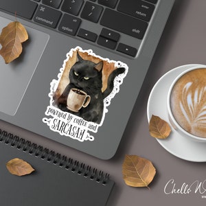 Puede incluir: Una pegatina con un gato negro sosteniendo una taza de caf&eacute;, con el texto "powered by coffee and sarcasm". La pegatina est&aacute; en un port&aacute;til, junto a una taza de caf&eacute; con arte latte y hojas de oto&ntilde;o.