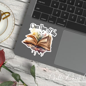 May include: A watercolor sticker featuring an open book with flowers and the text "Once Upon A Time". The sticker is on a laptop computer.