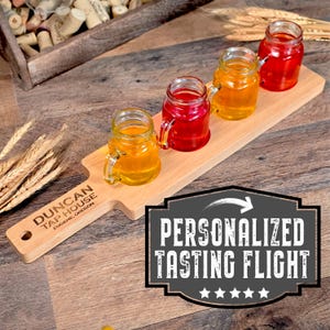 May include: A wooden tasting flight paddle with four small mason jar glasses filled with red and yellow liquids. The paddle is engraved with the text "Duncan Tap House, Eugene, Oregon". The paddle is labelled "Personalized Tasting Flight" with five stars.