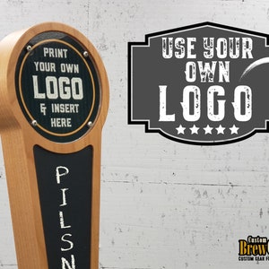 May include: A wooden beer tap handle with a black chalkboard insert. The chalkboard has the word "PILS" written on it. The top of the handle has a round, clear plastic insert with a black background and white text that reads "PRINT YOUR OWN LOGO & INSERT HERE". A gray sign with white text reads "USE YOUR OWN LOGO" with five white stars below the text.