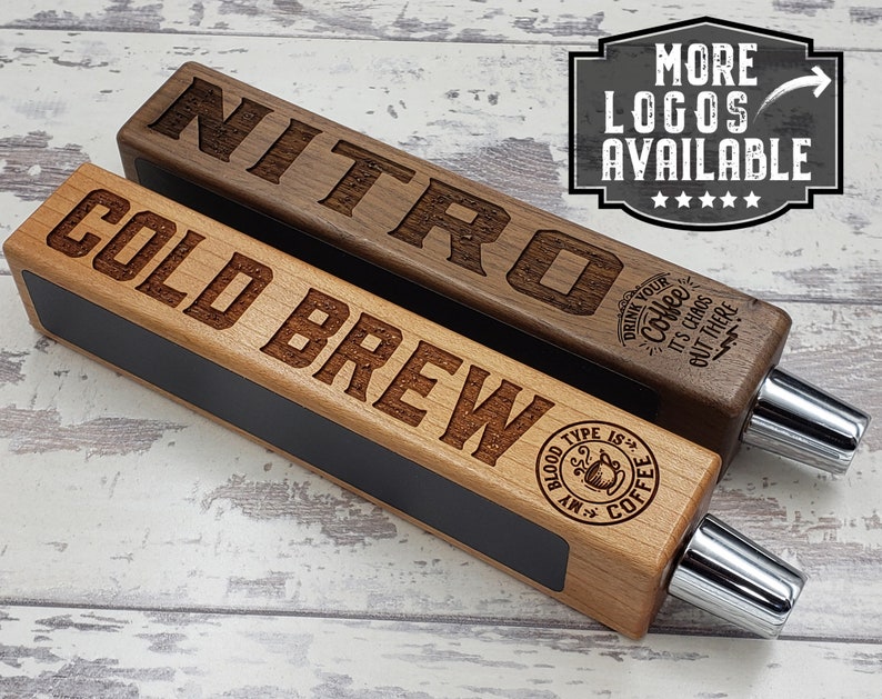 May include: Two wooden beer tap handles with engraved text. The top handle is walnut wood and says "NITRO" with a coffee cup design and the text "Drink your coffee, it's chaos but there". The bottom handle is light wood and says "COLD BREW" with a coffee cup design and the text "My blood type is coffee".