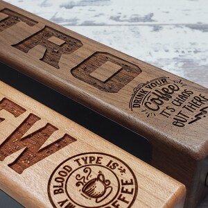May include: Two wooden beer tap handles with engraved text. The top handle is walnut and says "Drink your coffee it's chaos out there". The bottom handle is light wood and says "Brew" with a coffee cup logo that says "My blood type is coffee".