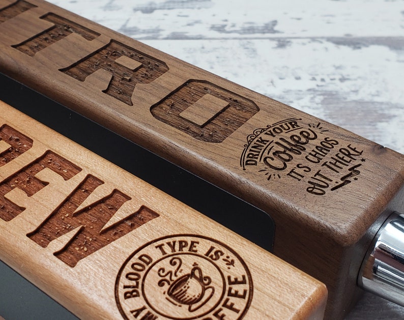 May include: Two wooden beer tap handles with engraved text. The top handle is walnut and says "Drink your coffee it's chaos out there". The bottom handle is light wood and says "Brew" with a coffee cup logo that says "My blood type is coffee".