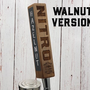 May include: A wooden tap handle with the word "NITRO" engraved on the front and "HAZELNUT" written on the side. The tap handle is made of walnut wood and has a black chalkboard surface. The text "DRINK YOUR COFFEE IT'S CHAOS OUT THERE" is engraved on the bottom of the tap handle.