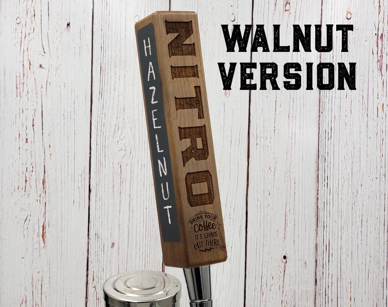 May include: A wooden tap handle with the word "NITRO" engraved on the front and "HAZELNUT" written on the side. The tap handle is made of walnut wood and has a black chalkboard surface. The text "DRINK YOUR COFFEE IT'S CHAOS OUT THERE" is engraved on the bottom of the tap handle.