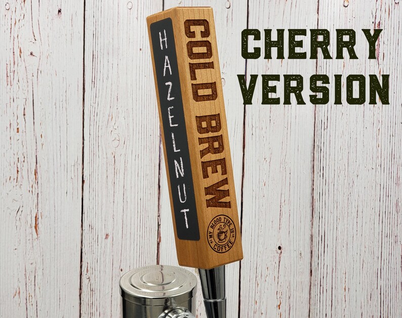 May include: A wooden beer tap handle with the words "COLD BREW" and "HAZELNUT" written on it. The handle also has a logo that says "My Blood Type is Coffee". The text "CHERRY VERSION" is written in green letters on a white wooden background.