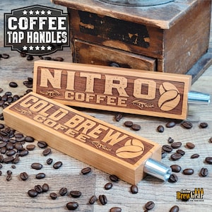 May include: Two wooden coffee tap handles with engraved text. The top handle reads "NITRO COFFEE" and the bottom handle reads "COLD BREW COFFEE". Both handles feature a coffee bean design.