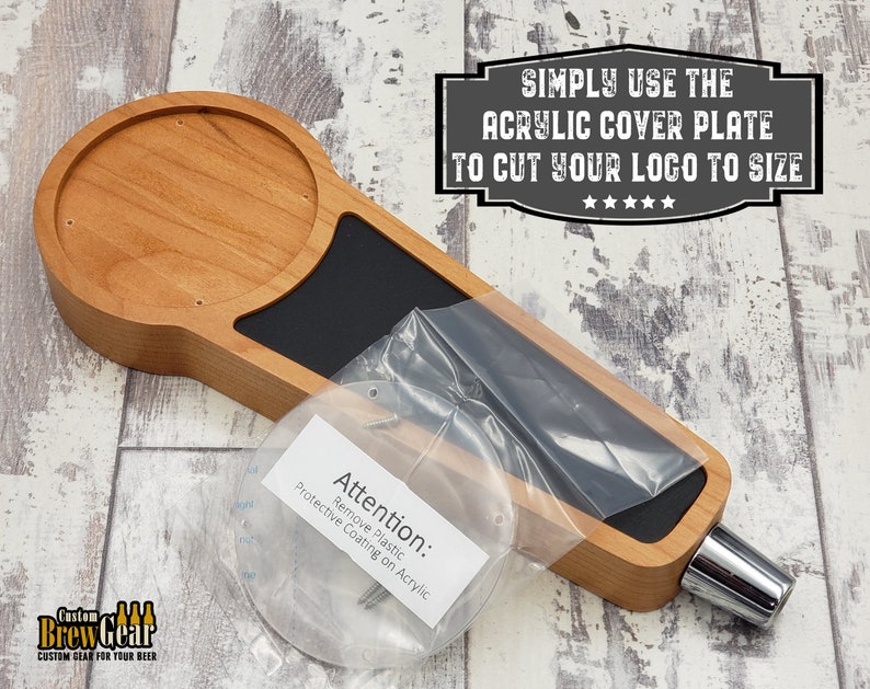 May include: A wooden beer tap handle with a round, unfinished wood top and a black, rectangular area for a logo. The handle comes with a clear acrylic cover plate and screws for attaching the logo. The text "SIMPLY USE THE ACRYLIC COVER PLATE TO CUT YOUR LOGO TO SIZE" is printed on a black sign above the handle. The text "Attention: Remove Plastic Protective Coating on Acrylic" is printed on a white label.