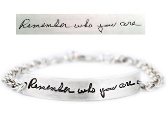 May include: Silver bracelet with a chain link design and a silver bar charm engraved with the handwritten message "Remember who you are."