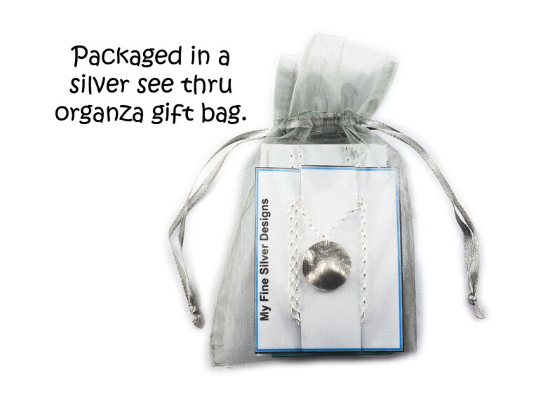 May include: A silver necklace with a textured, circular pendant is displayed inside a sheer, silver organza gift bag. The bag is tied with a matching ribbon. The text "My Fine Silver Designs" is visible on a card.