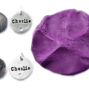 May include: Four small, round, silver-colored pendants with textured surfaces and a purple blob of clay. Two pendants have the name "Charlie" stamped on them. The pendants have a small loop for attaching to a chain or collar.