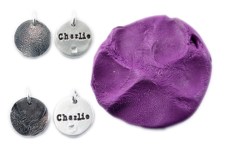 May include: Four small, round, silver-colored pendants with textured surfaces and a purple blob of clay. Two pendants have the name "Charlie" stamped on them. The pendants have a small loop for attaching to a chain or collar.