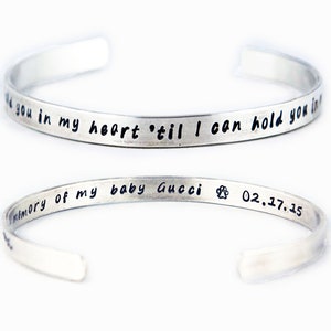 May include: Silver bracelet with the inscription "I'll you in my heart 'til I can hold you in memory of my baby Gucci 02.17.15" and a paw print.