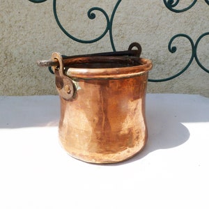 May include: A vintage copper pot with a metal handle. The pot has a hammered finish and is in good condition.