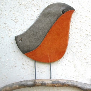 May include: A ceramic bird sculpture with a gray and orange glaze. The bird is perched on a branch.