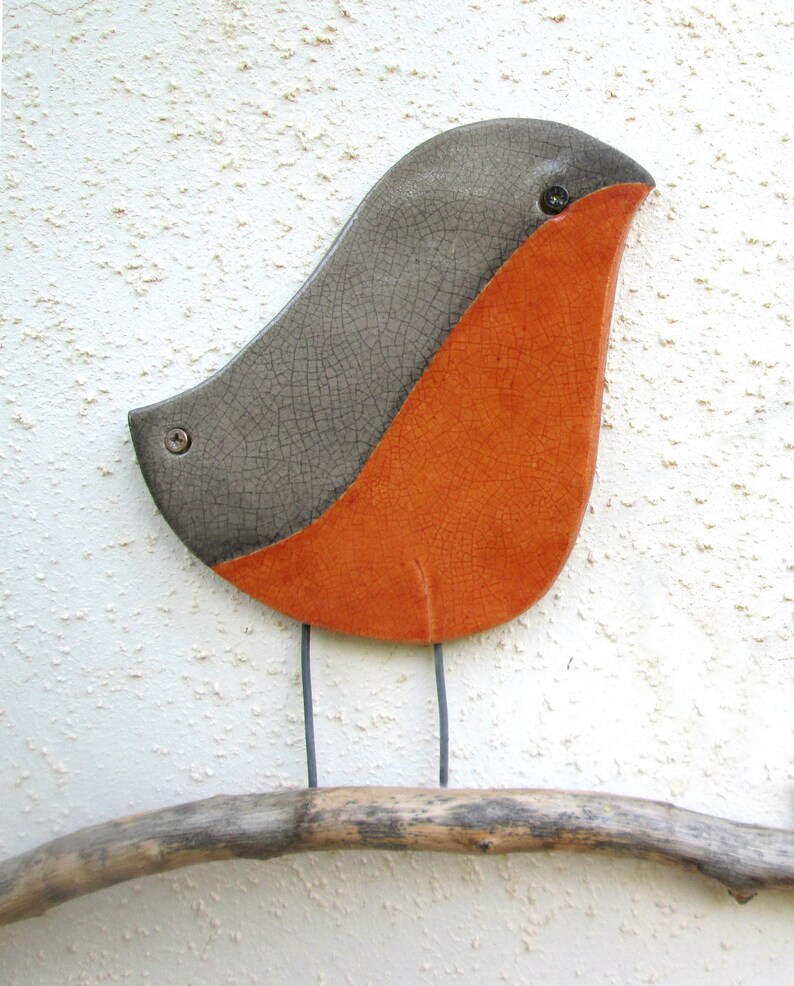 May include: A ceramic bird sculpture with a gray and orange glaze. The bird is perched on a branch.