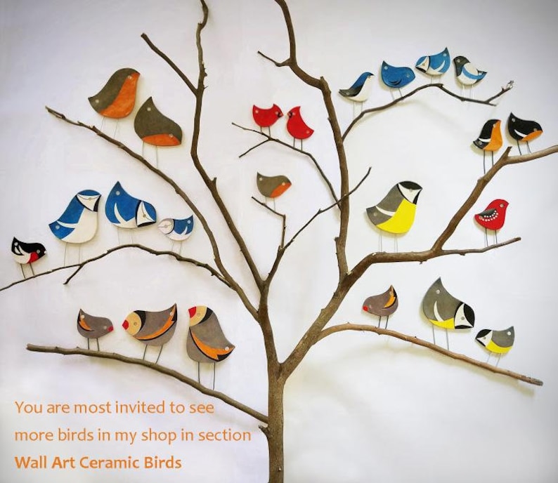 Op de afbeelding: Een verzameling keramische vogels in verschillende kleuren en ontwerpen zitten op een kale tak tegen een witte achtergrond. De vogels zijn geschilderd met felle kleuren, waaronder rood, blauw, geel en groen. De tekst "You are most invited to see more birds in my shop in section Wall Art Ceramic Birds" staat onder de afbeelding.