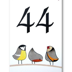 Op de afbeelding: Een wit keramisch huisnummerbord met het nummer 44 in zwarte schrijfletters. Drie cartoonvogels zitten op een tak aan de onderkant van het bord. De vogels zijn geel, grijs en grijs met oranje accenten.