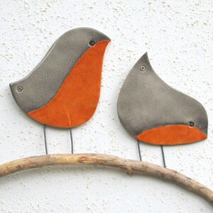 May include: Two ceramic birds with orange bellies perched on a branch. The birds are gray with a crackled glaze finish.